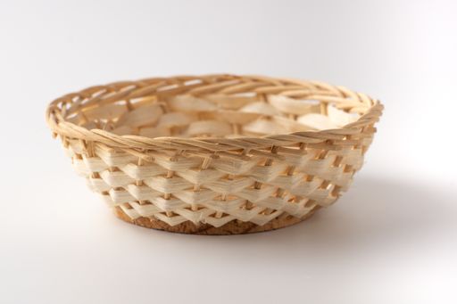 A round beige basket made with thatch isolated on the white background