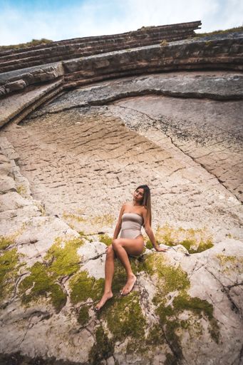 A vertical shot of a young female wearing a gray swimsuit and posing on the cliffs under the sunlight
