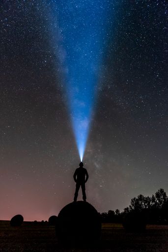 A silhouette of a male with a ray of light from the flashlight standing under the starry sky