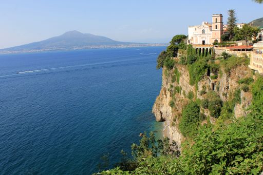 A beautiful view of a cliff on the Gulf of Naples, a small beach below, blue sea and Vesuvius on the horizon.