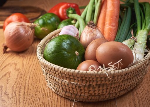 A  closeup shot of a basket with fresh vegetables and eggs on a brown table