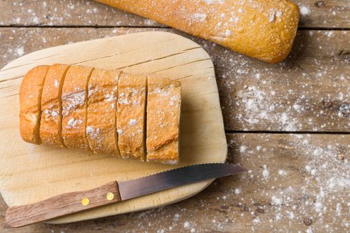 A overhead shot of a french bread cut in slices and a knife placed on a wooden board