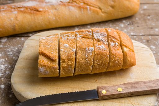 A overhead shot of a french bread cut in slices and a knife placed on a wooden board