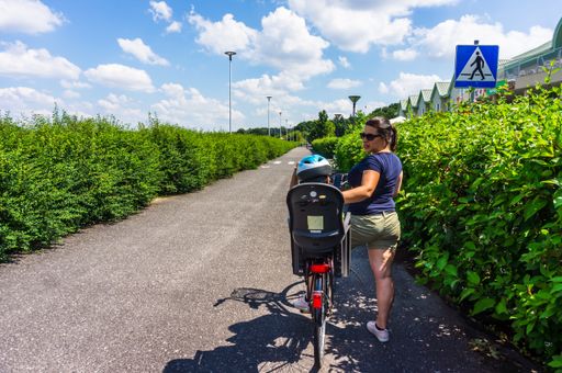 Woman and child in a safety seat with bicycle on a pathway at the Malta park on a sunny day
