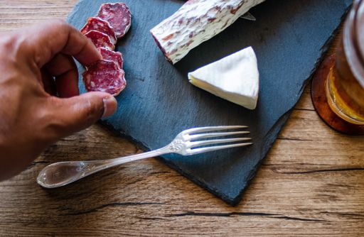 A closeup shot of brie cheese and smoked sausage on a board