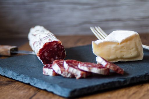 A closeup shot of brie cheese and smoked sausage on a board