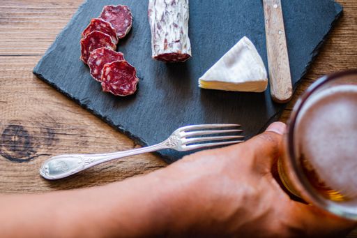 A closeup shot of brie cheese and smoked sausage and beer on a board