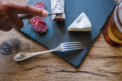 A closeup shot of brie cheese and a man cutting smoked sausage on a board