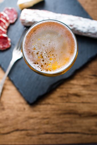 A vertical shot of beer brie cheese and smoked sausage on a board