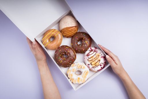 An overhead shot of a female holding a white box of different types of tasty donuts