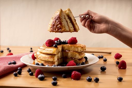 A closeup shot of a female taking a piece of pancakes with fresh berries on top