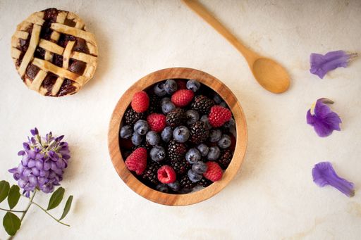 An overhead shot of a wooden bowl of fresh berries on a wooden table in a beautiful set