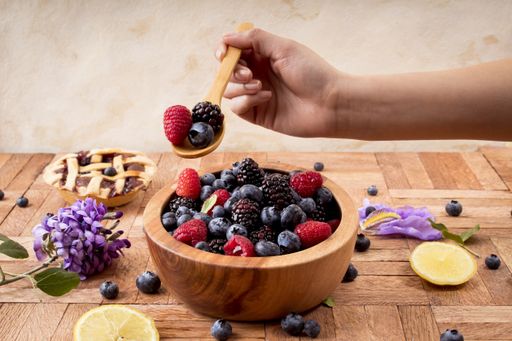A closeup shot of a  female taking a spoonful of berries from a wooden bowl