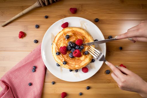 An overhead shot of a female taking a piece of pancakes with fresh berries on top