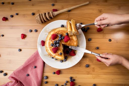 An overhead shot of a female taking a piece of pancakes with fresh berries on top
