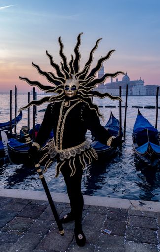 A vertical shot of a male wearing a black costume and an exotic mask standing by the sea