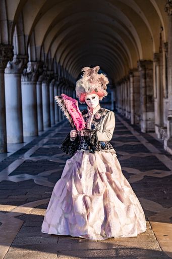 A vertical shot of a female wearing a black and pink costume and a mask standing in an old building
