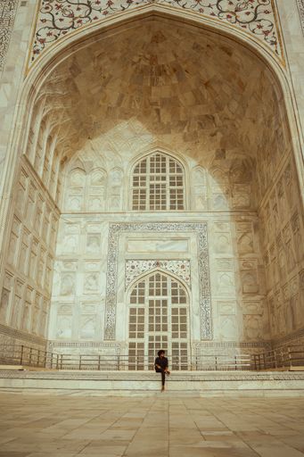 A vertical shot of a man sitting at the tomb entrance of Taj Mahal. Agra, India.