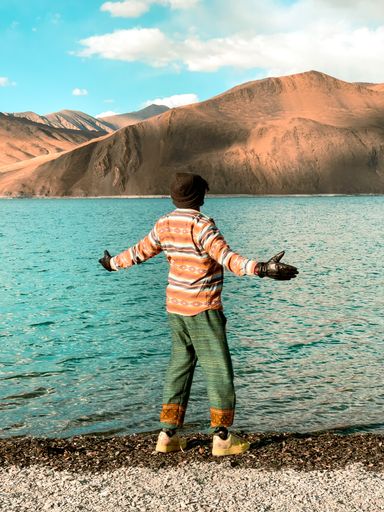 A vertical shot of a man standing on the shore of Pangong lake enjoying the view. Ladakh, West Tibet.