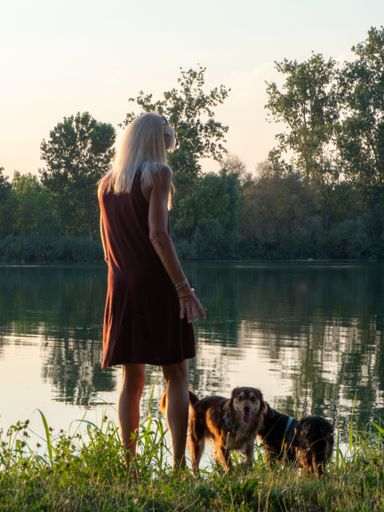 A blonde beautiful woman in a dress enjoying the view near a river accompanied by her dogs at sunset