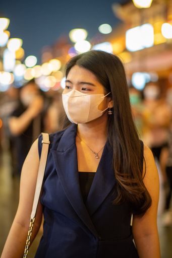 A vertical shot of a young stylish female with a mask on a bokeh city background
