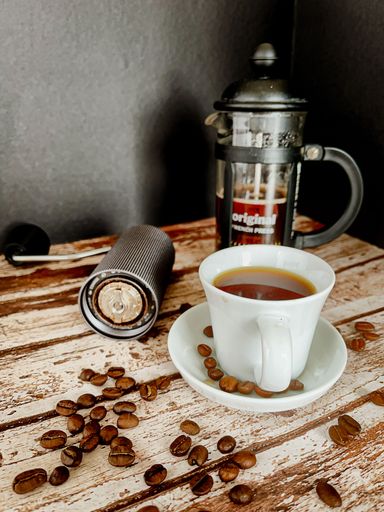 A vertical shot of a cup of coffee next to a French press coffee pot