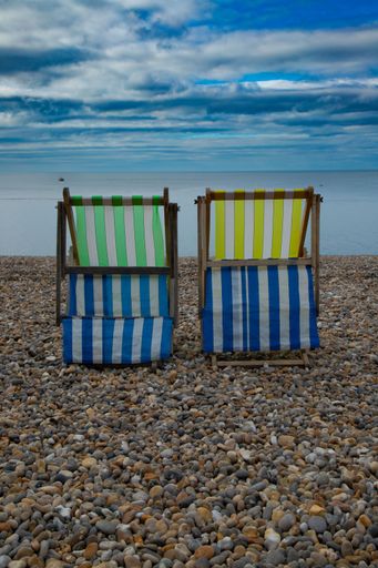 A vertical shot of two striped sunbeds on a rocky beach