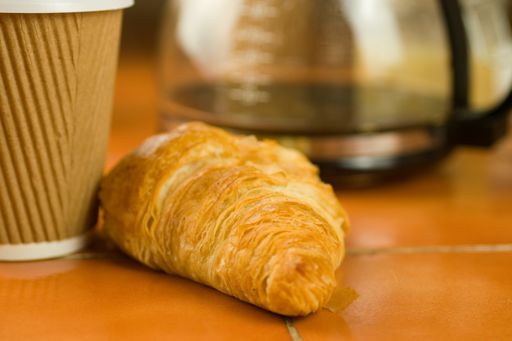 A selective focus shot of a croissant with takeaway coffee cup