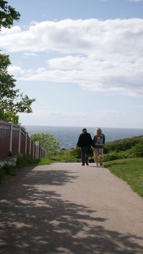 A vertical shot of two females seen from behind walking on a pathway surrounded by greenery