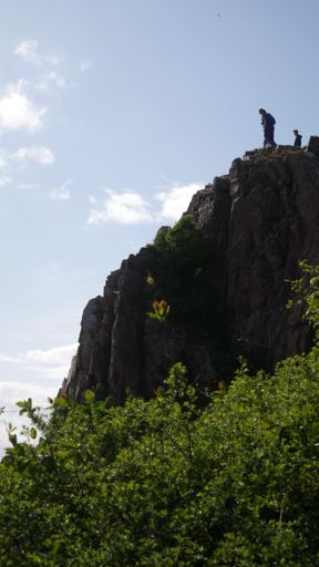 A low angle shot of people hiking on rocky mountains covered with greenery