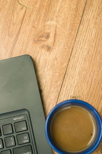 A vertical shot of a laptop with a blue mug of coffee on a wooden table
