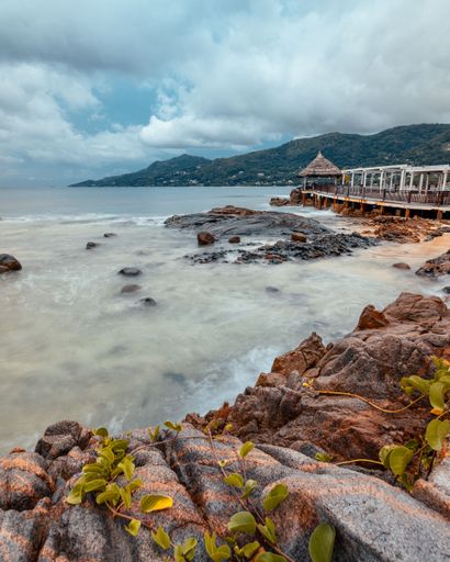 A vertical shot of a long exposure sea with mountainous forests in the background during daytime