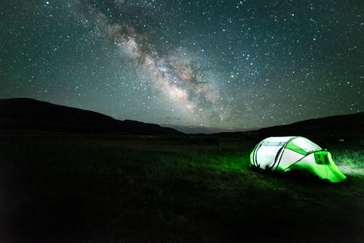 An illuminated green tent in the valley under bright starry sky