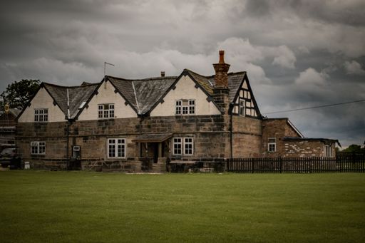 An old residential building on a green field in Wilmslow, the United Kingdom in cloudy sky background
