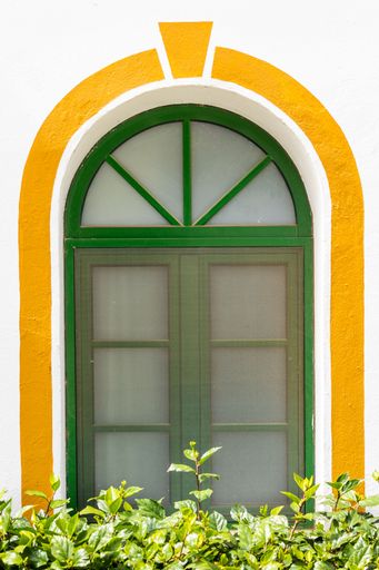 A vertical shot of a decorative arched green window with a yellow outline
