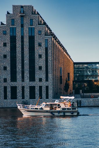 A vertical shot of a small yacht in front of a nice modern building in Berlin, during sunset