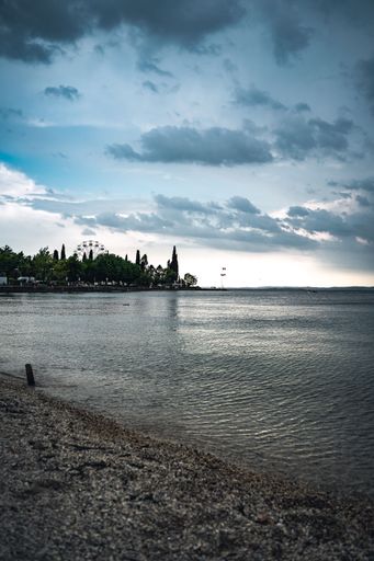 A vertical shot from the shore of dark clouds in blue sky reflected in Lake Garda in Bardolino, Italy