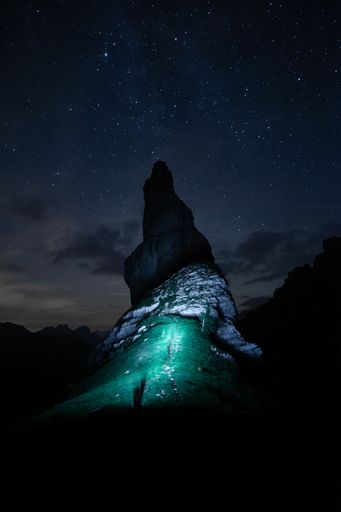 A vertical shot of a green light near a stone formation under a starry night sky in Campanile di Val Montanaia, Italy