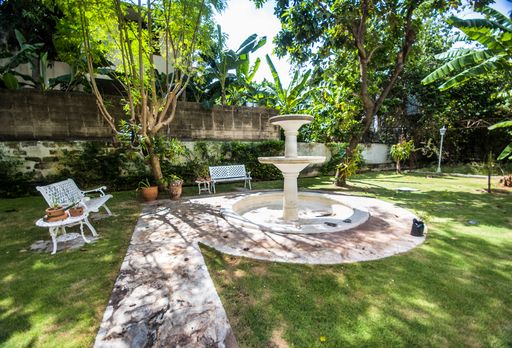 A beautiful decorative backyard of a house with a fountain, seats, plants and trees