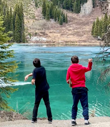 A vertical shot of two boys throwing rocks into the Emerald Lake near a road to the mountains