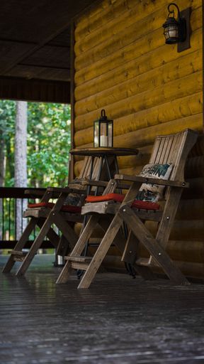 A vertical shot of the wooden chairs near the wooden house