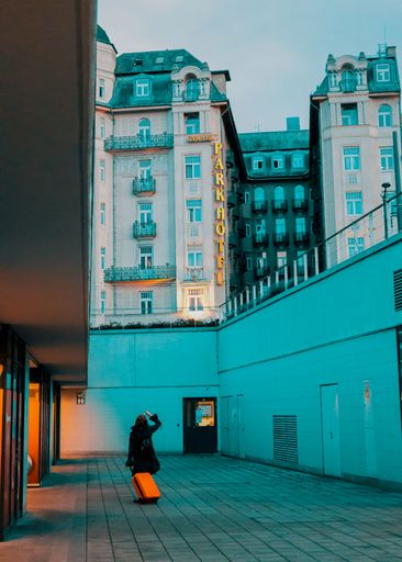 A vertical shot of a female standing with a bagage looking at the "Grand Park" hotel in Budapest