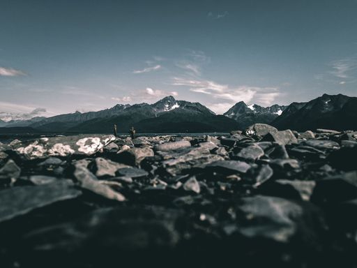 A beautiful shot of snowy mountains from a rocky pond shore in Alaska