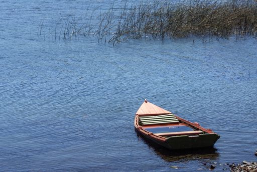 A high angle shot of a small boat on the calm water, near the shore during daylight