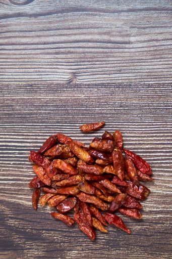 A vertical high angle shot of a pile of red chili peppers on a wooden surface