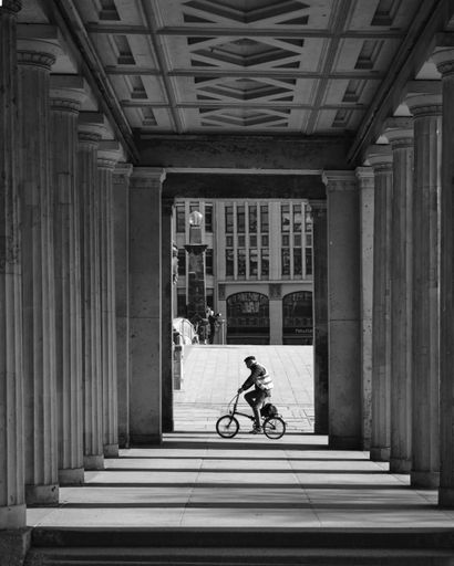 A grayscale shot of a cyclist between columns of Altes Museum in Berlin, Germany