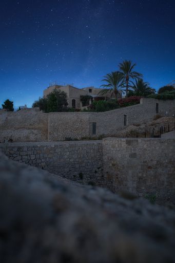 A vertical shot of an old fortress under a starry blue sky with tropical trees