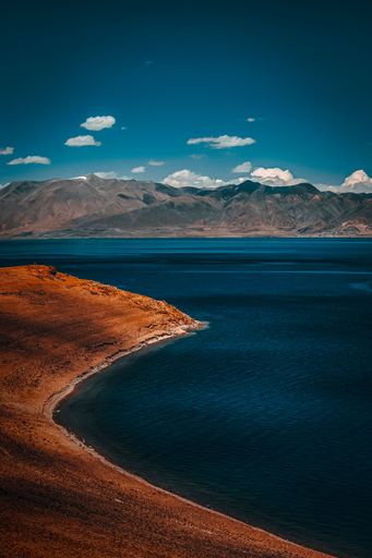 A vertical bird's eye view of a red sandy beach with a background of mountains