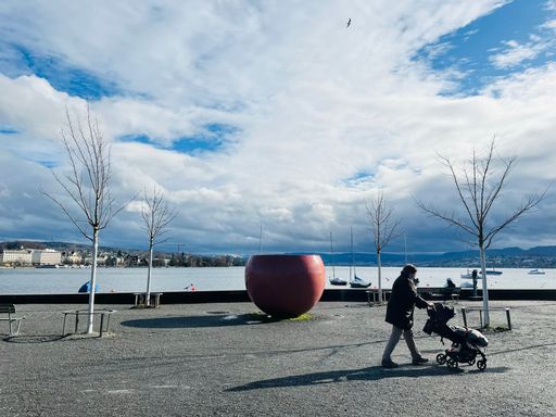 A side view of a woman with baby carriage walking on the lakeshore on blue cloudy sky background