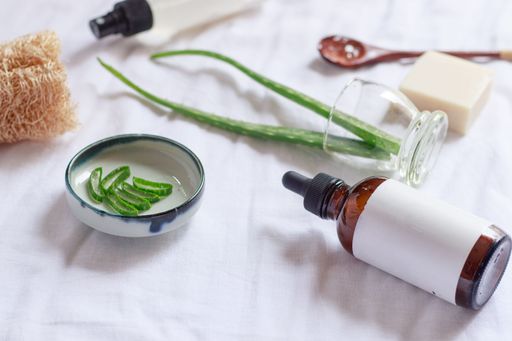 A closeup of a brown glass bottle around aloe leaves on a white cloth